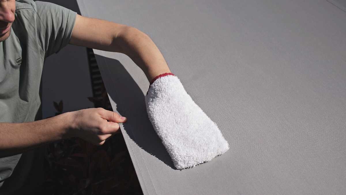 Reinigung einer Markise mit einem Wasch-Handschuh Person reinigt eine graue Oberfläche mit einem weißen Handschuh